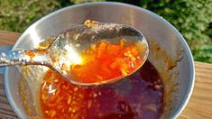 a spoon filled with liquid sitting on top of a metal bowl next to a wooden table