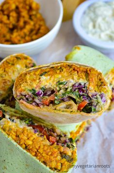 two burritos stacked on top of each other in front of bowls of food