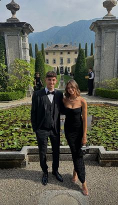 two people in formal wear standing next to each other near water lilies and trees