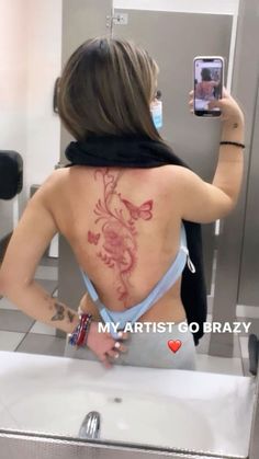 a woman taking a selfie in the mirror with her cell phone and tattoo on her back