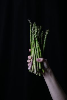 a person holding asparagus in their hand on a black background