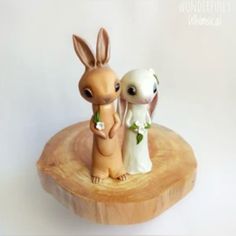 two small figurines sitting on top of a piece of wood