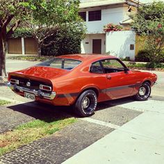 an orange muscle car parked on the side of the road in front of a house