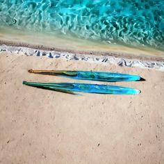 two blue and green brushes laying on the sand next to an ocean beach with waves coming in