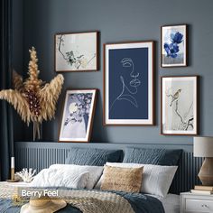 a bedroom with blue walls and pictures hanging on the wall above the bed, along with a wicker basket full of dried flowers