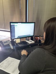 a woman sitting in front of a computer on top of a desk next to a phone