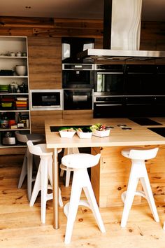 a kitchen with wooden flooring and white stools next to a table in front of an oven