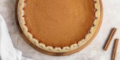 a pumpkin pie on a wooden plate with two cinnamon sticks