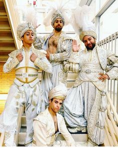 four men dressed in white and gold standing next to each other on the steps with their hands up