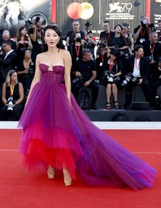 a woman in a purple and red dress standing on a red carpet with photographers behind her