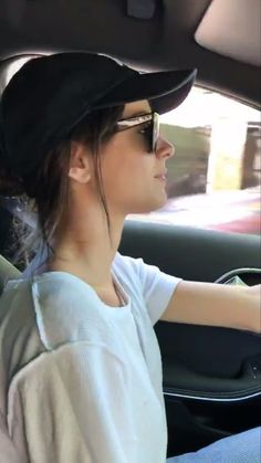 a woman driving a car with her hand on the steering wheel while wearing sunglasses and a black hat