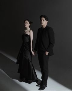 a man and woman standing next to each other in front of a dark background wearing black clothing