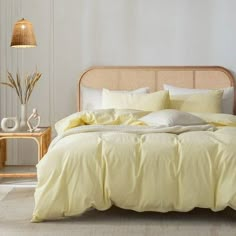 a bed with yellow sheets and pillows in a white room next to a wicker headboard