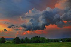 the sky is filled with clouds as the sun sets over a green field and trees