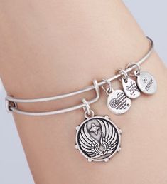 a woman wearing a silver bracelet with two charms on the wrist and an angel charm