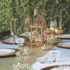 a table set with plates, candles and a birdcage on top of it