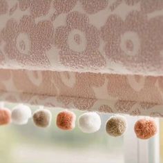 some balls are hanging from a window sill in front of a curtain with pink and white fabric