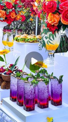 there are many drinks on the table with flowers in vases and plates full of food