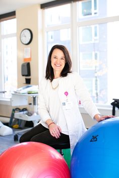 a woman sitting on top of three exercise balls in a room with large windows behind her