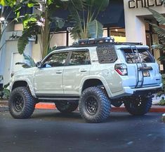 a white four - doored suv parked in front of a building with large tires