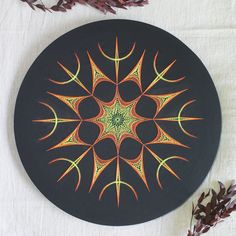 a black plate with an orange and green design on it next to some purple flowers