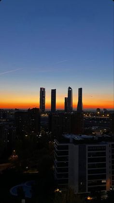 the sun is setting in front of some tall buildings and skyscrapers with planes flying overhead