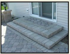 a brick patio with steps leading up to the front door and side window in the background