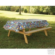 a picnic table cover with cars and trucks on it sitting in the middle of a field