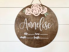 a wooden sign hanging on the side of a white wall with pink flowers and name