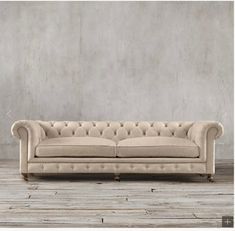 an old style couch in front of a concrete wall with wooden flooring and white walls