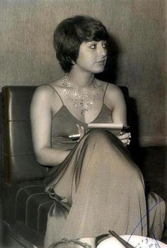 an old photo of a woman sitting in a chair with a book on her lap