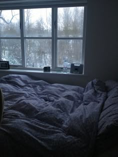 an unmade bed sitting next to a window in a room with snow on the ground