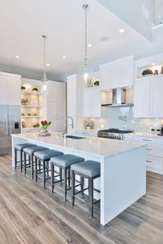 a large kitchen with white cabinets and counter tops, an island in the middle is flanked by four stools