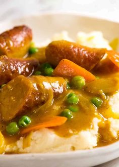 a white bowl filled with mashed potatoes and meat covered in gravy, peas and carrots