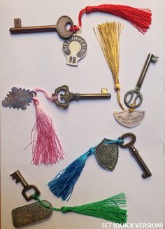 an assortment of antique keys are displayed on a white surface with red, green and blue tassels