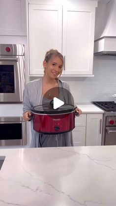 a woman standing in a kitchen holding a red crock pot