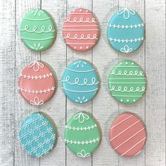 decorated cookies are arranged in rows on a white table with wood planks and painted eggs