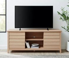 a flat screen tv sitting on top of a wooden entertainment center next to a potted plant