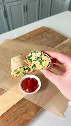 a person is holding a burrito in their hand with ketchup on the side