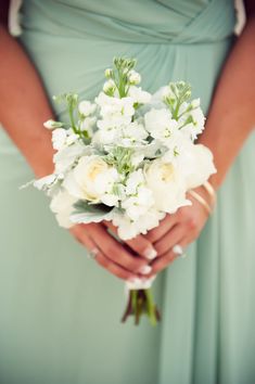 a woman in a blue dress holding a bouquet of white flowers and greenery on her wedding day