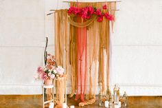 an arrangement of flowers and candles on a wooden table in front of a wall hanging from the ceiling