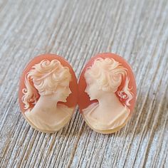 Very Lovely Vintage Cameo Earrings! 1980's/ 1990's  These oval shell carved earrings feature ivory colored lady with ponytail cameo on a peachy pink background. These are for pierced ears.  Measures 3/4" length, 1/2" width Great vintage condition. Does show signs of age.  Clean. No chips or cracks. Very lightweight. Posts are secure. See all photos  If you have any questions, please ask. 90s Earrings, Cameo Earrings, Cameo Jewelry, Vintage Cameo, Peachy Pink, Pierced Earrings, Ivory Color, Pierced Ears, Pink Background