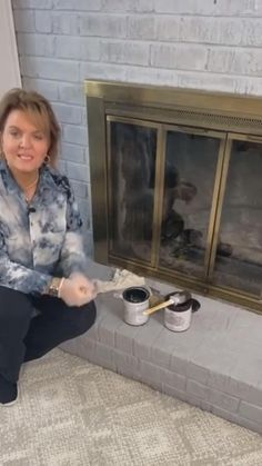 a woman sitting on the floor with paint in front of a fire place and fireplace