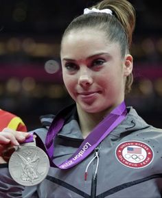 a woman in grey jacket holding up a silver medal