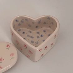 a heart shaped container next to a small box with flowers on it and a white background