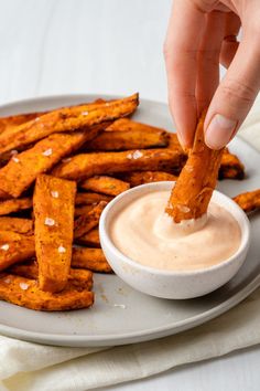 a person dipping some kind of sauce on sweet potato fries