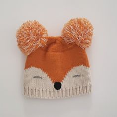 an orange and white knitted fox hat with pom - poms on it