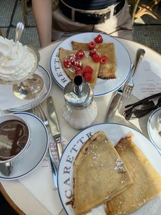 two plates with pancakes, whipped cream and berries on them are sitting on a table