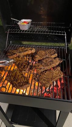 steaks cooking on an outdoor bbq grill, with a side dish for dipping sauce