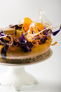 there is a cake with purple and orange toppings on the top, sitting on a white pedestal